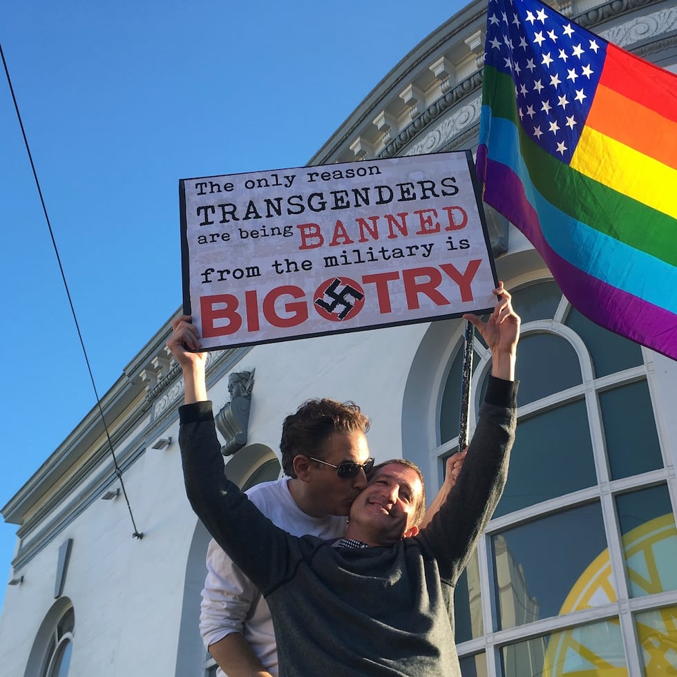 Nick Rondoletto, izquierda, y Doug Thorogood, ambos de San Francisco, ondean una bandera multicolor y sostienen un cartel durante una protesta realizada en San Francisco en 2017 para oponerse a una propuesta para prohibir que personas transgénero presten servicio en el Ejército de Estados Unidos.