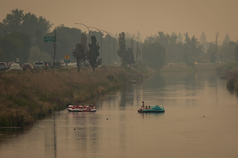 Varias personas flotan en el sendero Channel Pathway que conecta el lago Okanagan con el lago Skaha, mientras el humo de los incendios forestales que azotan la región llena el aire, en Penticton, Columbia Británica, el lunes 10 de agosto de 2026. (Darryl Dyck/The Canadian Press vía AP)