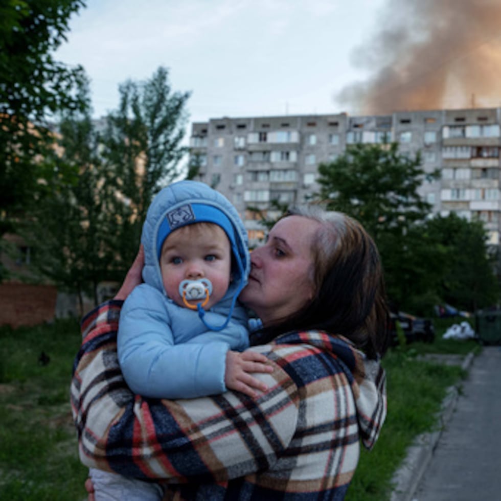 Una mujer lleva a un bebé en brazos cerca de un edificio residencial dañado por un ataque ruso, en Kiev.