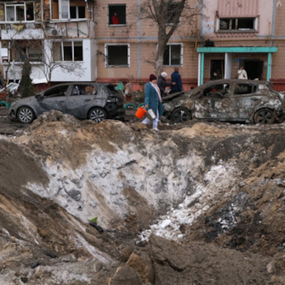 Varias personas pasan junto a un cráter y coches dañados cerca de un edificio de apartamentos tras un ataque ruso en Zaporizhzhia, Ucrania.