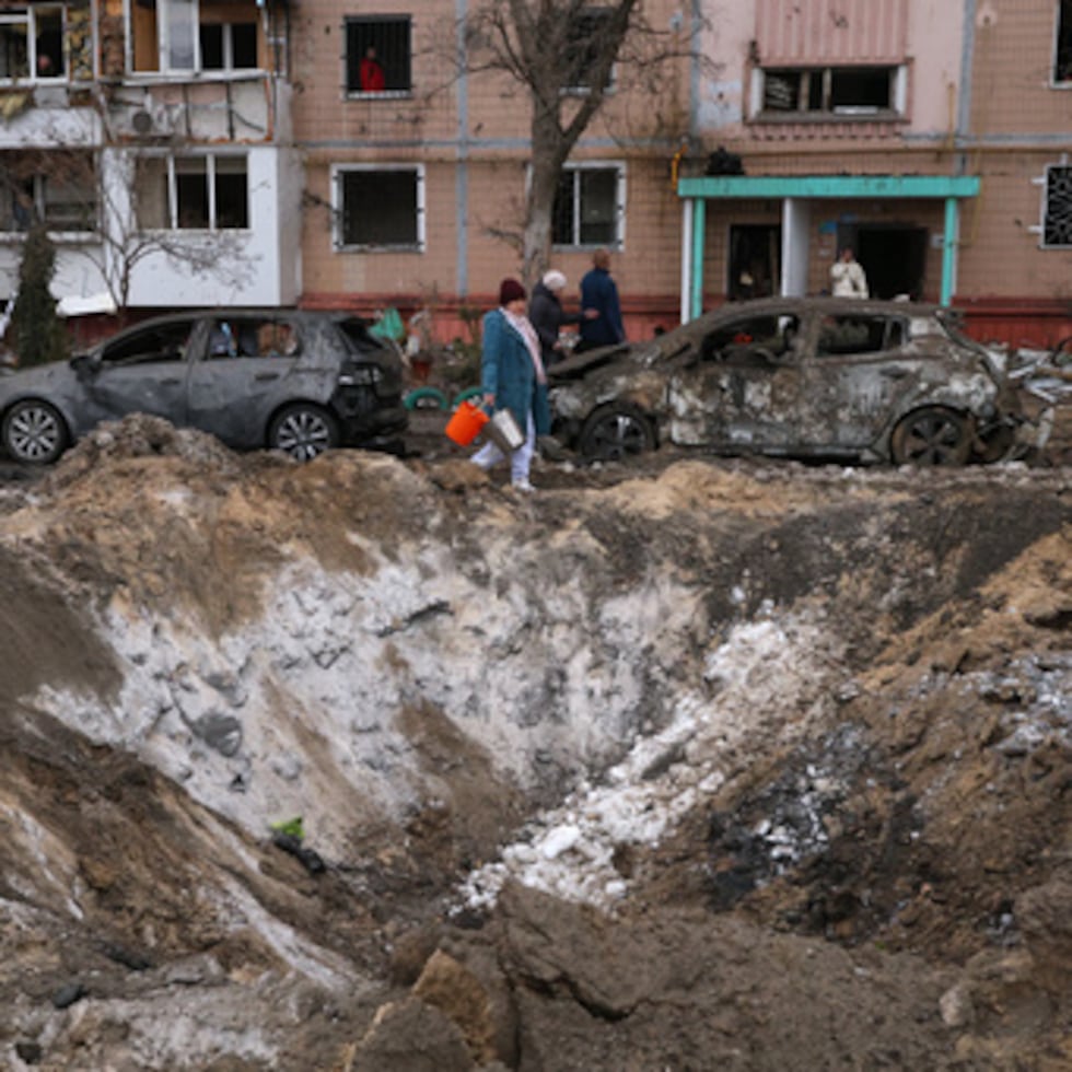 Varias personas pasan junto a un cráter y coches dañados cerca de un edificio de apartamentos tras un ataque ruso en Zaporizhzhia, Ucrania.