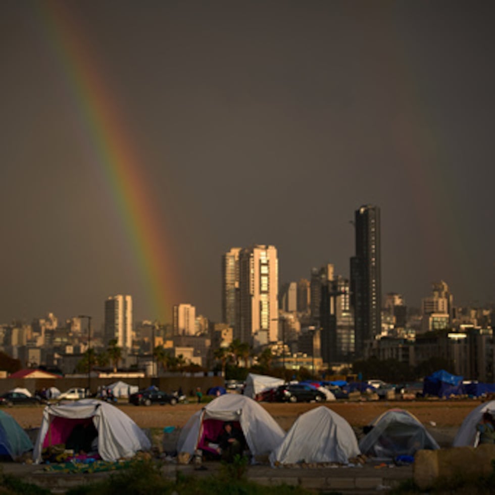 Desplazados que huyeron de los ataques israelíes en el sur del Líbano se sientan en el interior de tiendas de campaña utilizadas como refugios mientras un arco iris se abre paso a través de la lluvia en Beirut, Líbano, domingo 29 de marzo de 2026. (AP Photo/Emilio Morenatti)