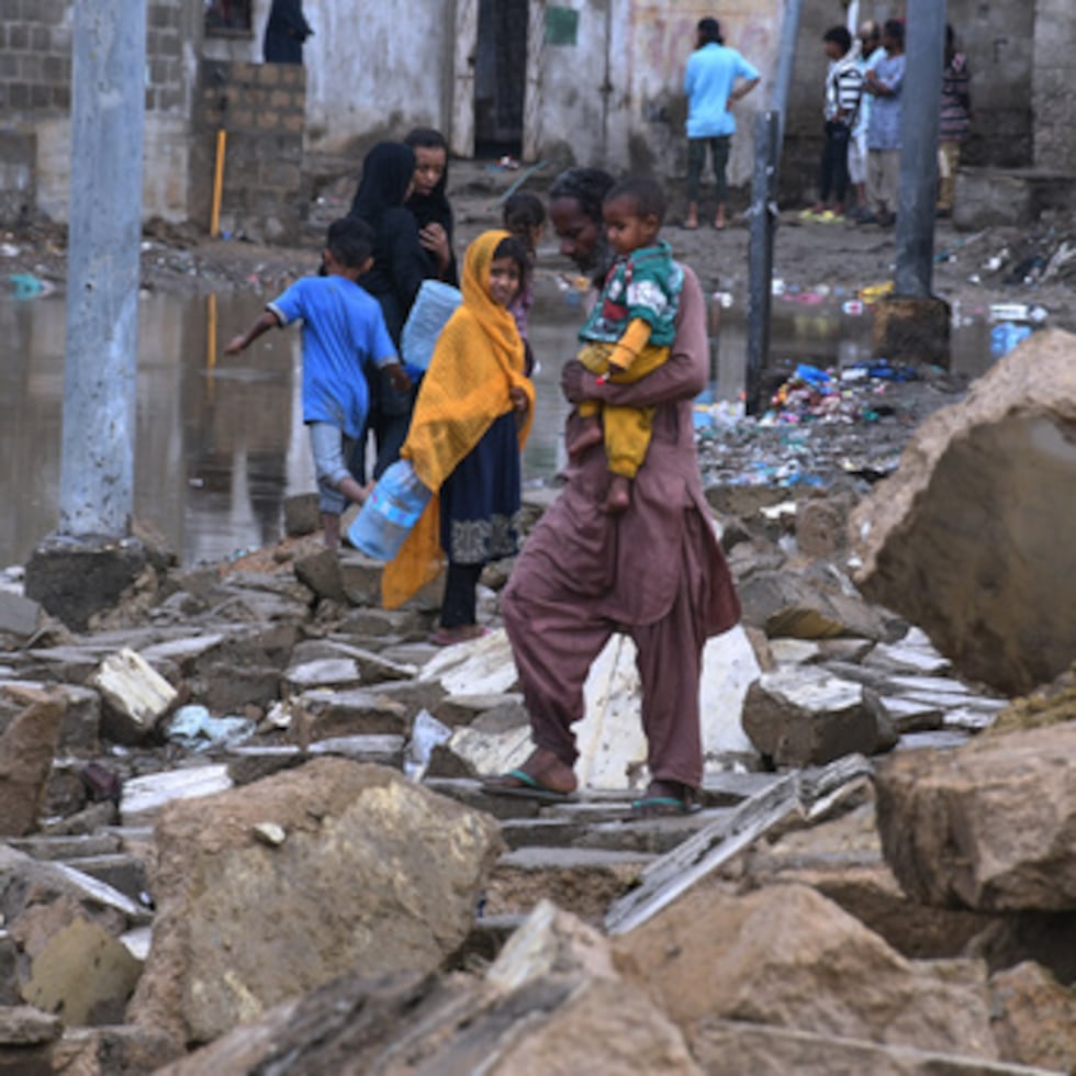 Vecinos pasan entre los escombros de un muro derrumbado por fuertes lluvias y viento en Karachi.