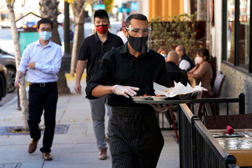 Un mesero y otras dos personas en el exterior con mascarilla en California.