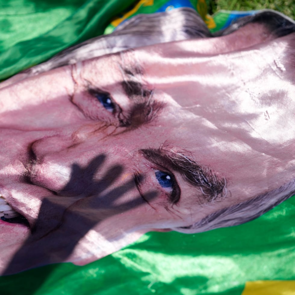 La sombra de un simpatizante del expresidente Jair Bolsonaro se proyecta sobre una imagen suya expuesta fuera del hospital donde fue trasladado de prisión para cirugía, en Brasilia, Brasil, el 24 de diciembre de 2025. (Foto AP/Eraldo Peres)