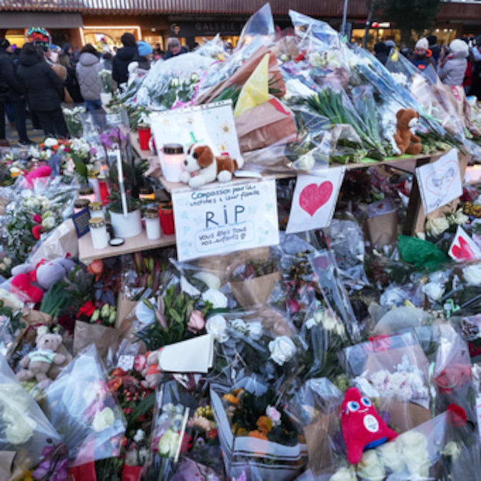 Varias personas rodean las ofrendas florales y las velas colocadas en el exterior del bar Le Constellation de Crans-Montana, en los Alpes suizos, Suiza, el sábado 3 de enero de 2026, donde un devastador incendio dejó muertos y heridos durante las celebraciones de Año Nuevo. (AP Photo/Antonio Calanni)