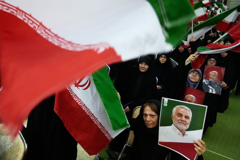 Mujeres ondean banderas nacionales mientras sostienen carteles del difunto comandante de la Fuerza Quds de la Guardia Revolucionaria de Irán, el general Qassem Soleimani, quien murió en un ataque con drones estadounidenses en 2020 en Irak, durante una ceremonia en conmemoración del aniversario de su muerte en la gran mezquita Imán Jomeini en Teherán, Irán, el jueves 1 de enero de 2026. (Foto AP/Vahid Salemi)