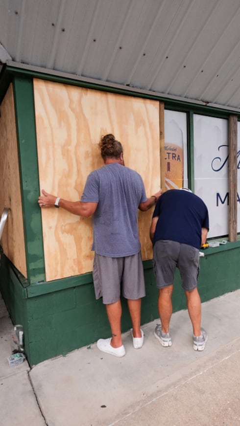 Joshua Brown, a la izquierda, y Mike Howard colocan paneles de madera para proteger el bar deportivo Perdido Key Sports Bar ante la proximidad del huracán Isaías a Perdido Key, Florida.