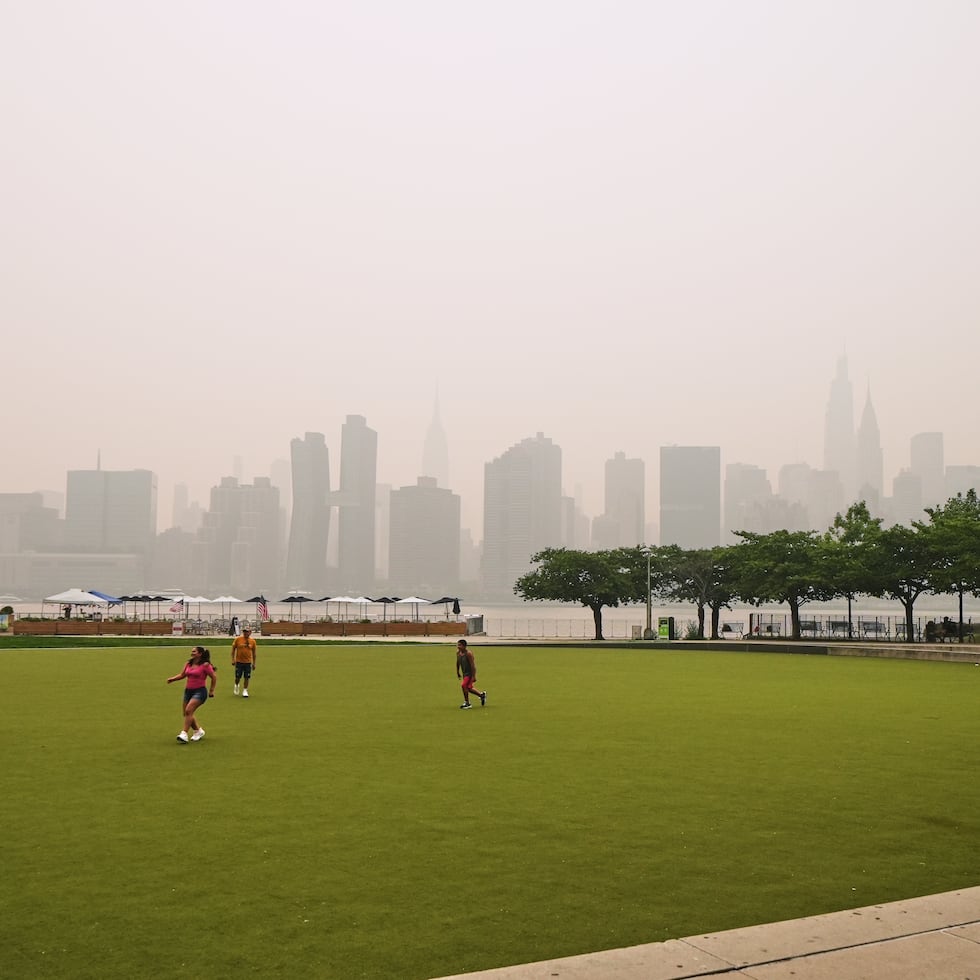 Un grupo de personas juega en el Hunter's Point South Park Athletic Field. Al fondo se aprecian los rascacielos de Nueva York, ocultos parcialmente por el humo de los incendios forestales en Canadá.