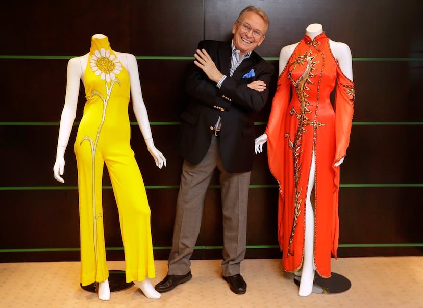 El diseñador de moda y vestuario Bob Mackie posa con dos de sus diseños emblemáticos: un vestido de satén rojo escarlata que lució Cher en 1975 (a la derecha) y un mono de jersey color caléndula que Cher llevó entre 1971 y 1976 (a la izquierda), en Londres, el 16 de agosto de 2018.