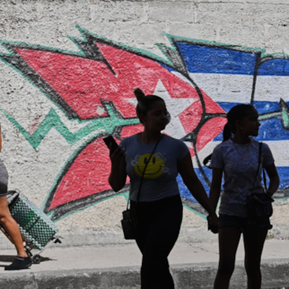 Varias personas pasan junto a unos grafitis con los colores de la bandera cubana en La Habana, Cuba.