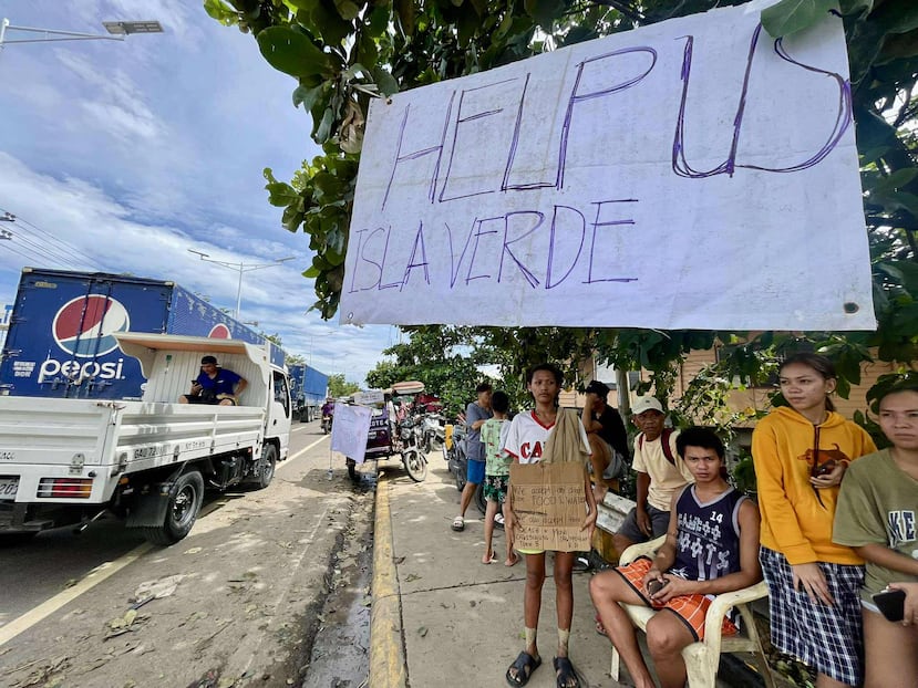 Los residentes de Isla Verde se encuentran junto a un cartel que ellos mismos hicieron para pedir ayuda mientras regresan a sus hogares dañados después de que el tifón Kalmaegi causara devastación en las comunidades a lo largo del río Mananga en la ciudad de Talisay, provincia de Cebú, en el centro de Filipinas.