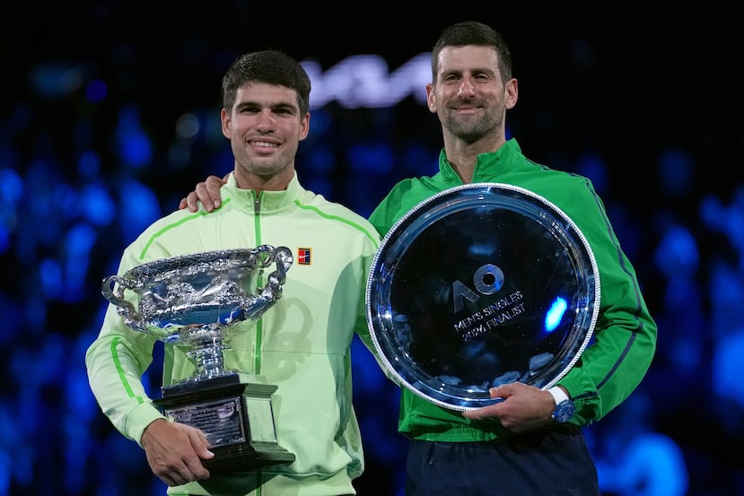 Carlos Alcaraz (izq) sostiene la copa de campeón del Abierto de Australia tras vencer a Novak Djokovic en la final de sencillos masculino.