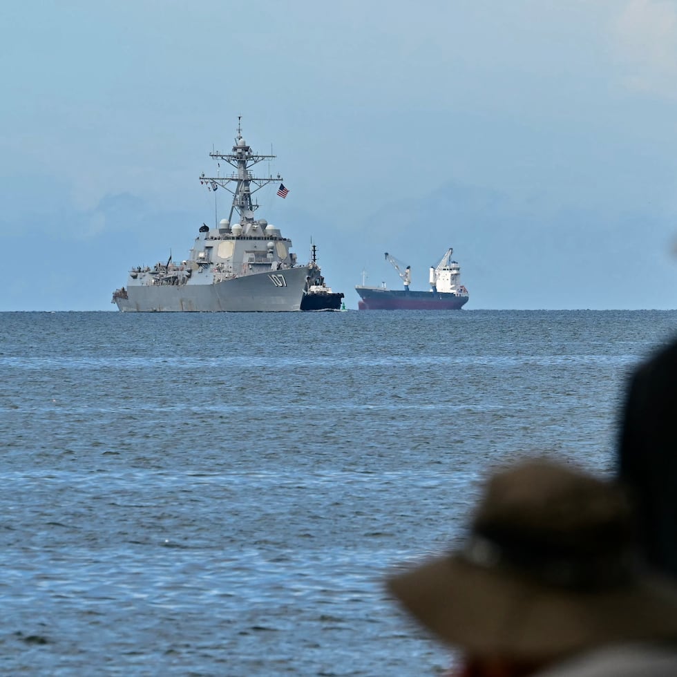 El buque de guerra USS Gravely se ve a lo lejos frente a la costa de Puerto España, mientras pescadores observan desde la capital trinitense.