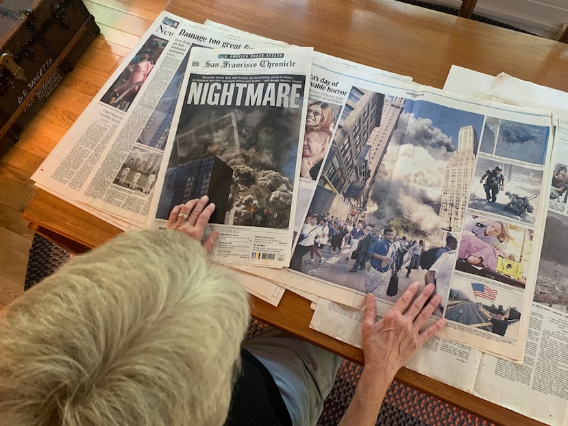 En esta imagen tomada con un celular, Amy Sancetta, fotógrafa jubilada de The Associated Press, observa recortes de periódico que muestran fotografías que ella tomó de los ataques del 11 de septiembre de 2001 contra el World Trade Center de Nueva York, el martes 1 de septiembre de 2026, en su casa cerca de Cleveland. (AP Foto/Mike Householder)