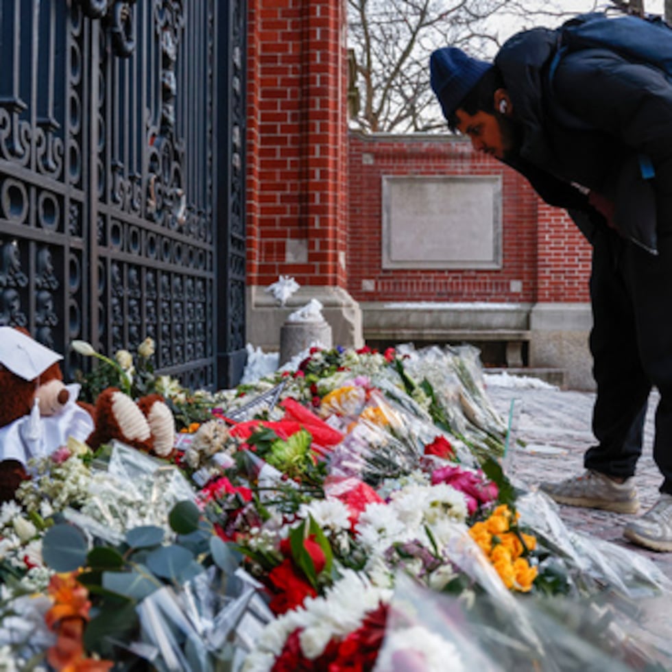 Un miembro de la comunidad mira las flores, notas y recuerdos en un monumento improvisado frente a las puertas Van Wickle de la Universidad Brown, en Providence, R.I., dos días después de un tiroteo que tuvo lugar en el campus de la universidad.