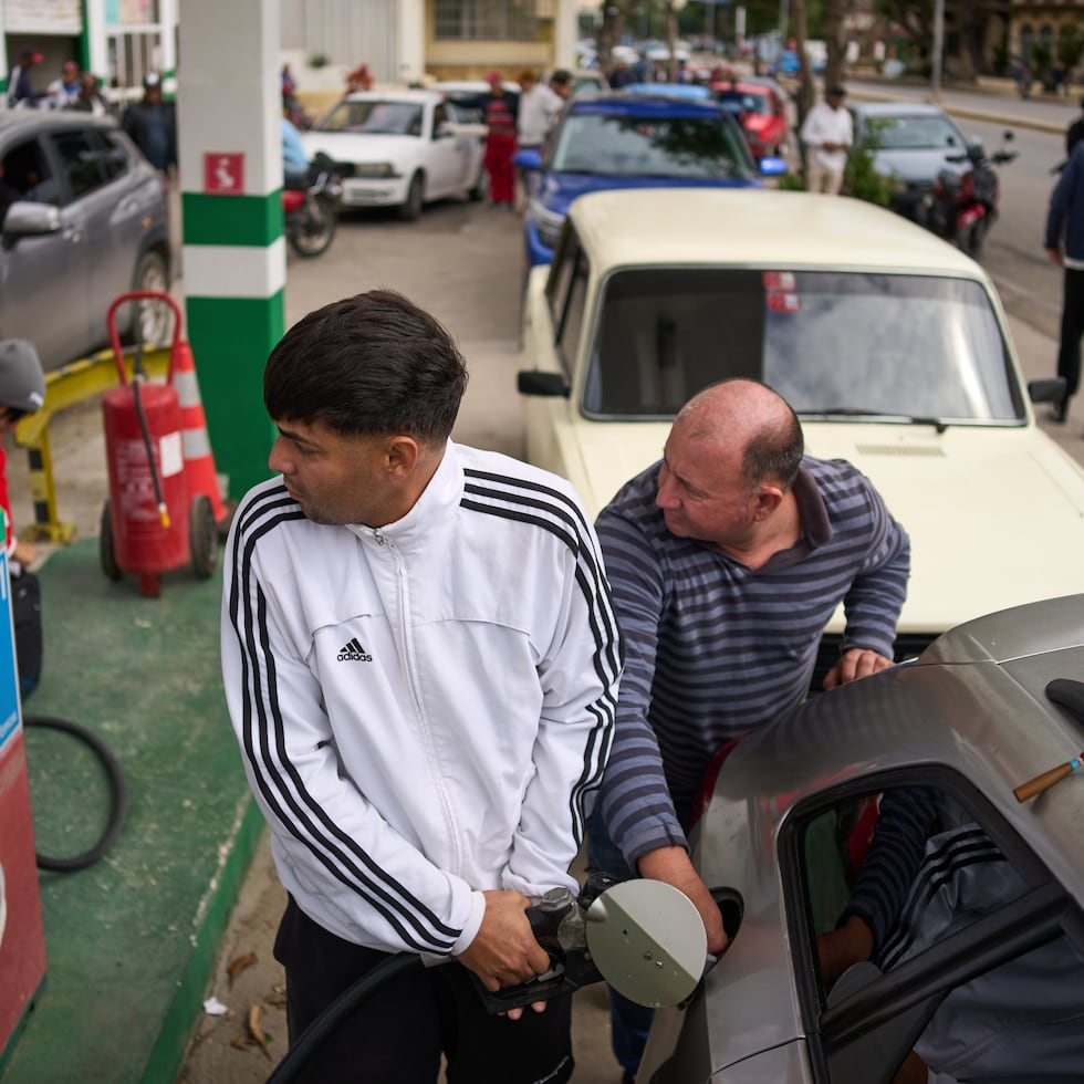 Personas repostan en una gasolinera mientras otros esperan detrás en una larga fila en La Habana, Cuba.