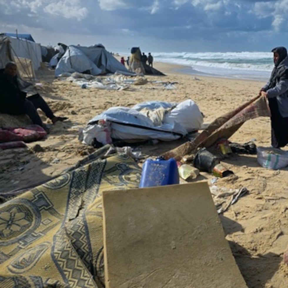 Una mujer intenta recuperar una alfombra después de que las lluvias de la noche anterior inundaran un campamento de tiendas junto a la playa en Khan Younis, en el sur de la Franja de Gaza, el domingo 28 de diciembre de 2025. (AP Photo/Mohammad Jahjouh)