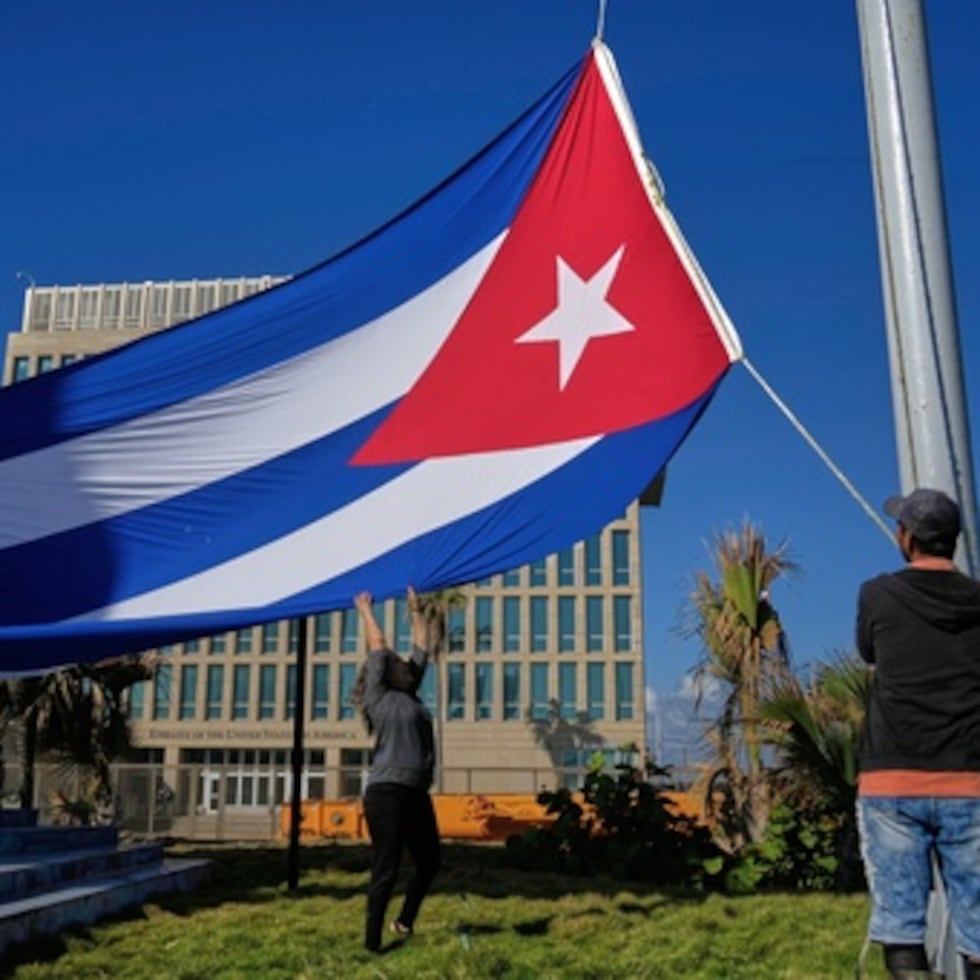 Trabajadores ondean la bandera cubana a media asta en la Tribuna Antiimperialista cerca de la Embajada de Estados Unidos en La Habana, Cuba, el lunes 5 de enero de 2026, en memoria de los cubanos que murieron dos días antes en Caracas, Venezuela, durante la captura del presidente venezolano Nicolás Maduro por fuerzas estadounidenses. (AP Photo/Ramon Espinosa)