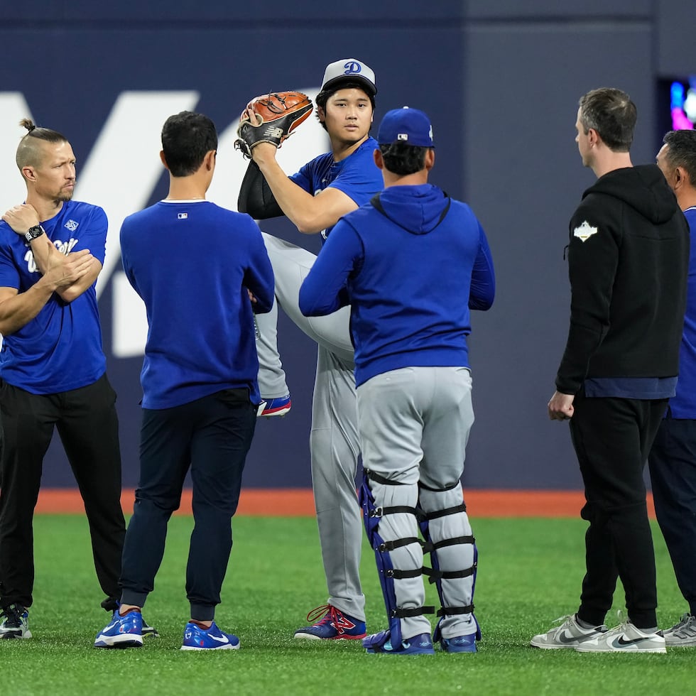 Shohei Ohtani, al centro, practica su movimiento para lanzar mientras conversa con personal del equipo.