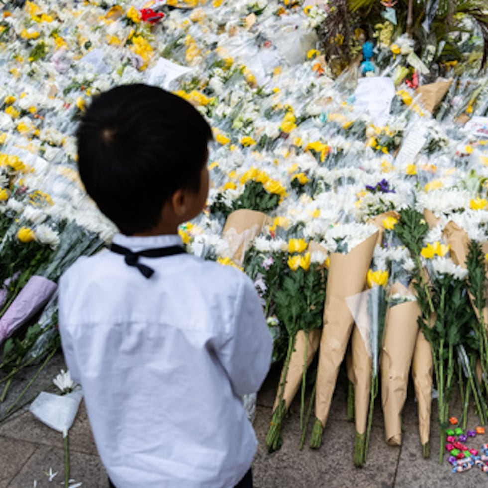 Un grupo de personas ofrece flores a las víctimas cerca del lugar donde se produjo un incendio mortal en Wang Fuk Court, una urbanización del distrito de Tai Po.