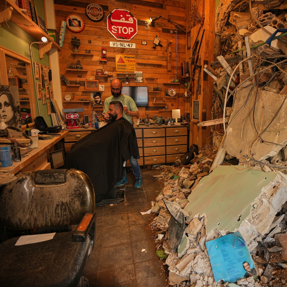 El barbero Mohammad Mehdi le corta el cabello a su cliente Ayman Al Zein dentro de su barbería, que resultó dañada en un ataque aéreo israelí que también dañó el local de Al Zein, en Dahiyeh, en los suburbios del sur de Beirut, Líbano.