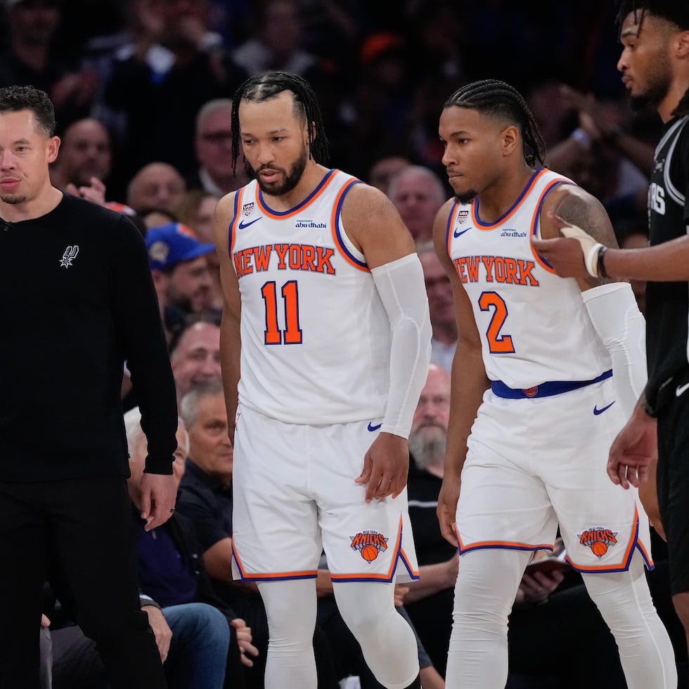 Jalen Brunson (11) y el escolta Miles McBride (2), de los Knicks, caminan hacia su banca mientras el entrenador de los Spurs, Mitch Johnson (izquierda), mira hacia otro lado durante la segunda mitad del tercer juego de las Finales de la NBA, el lunes.