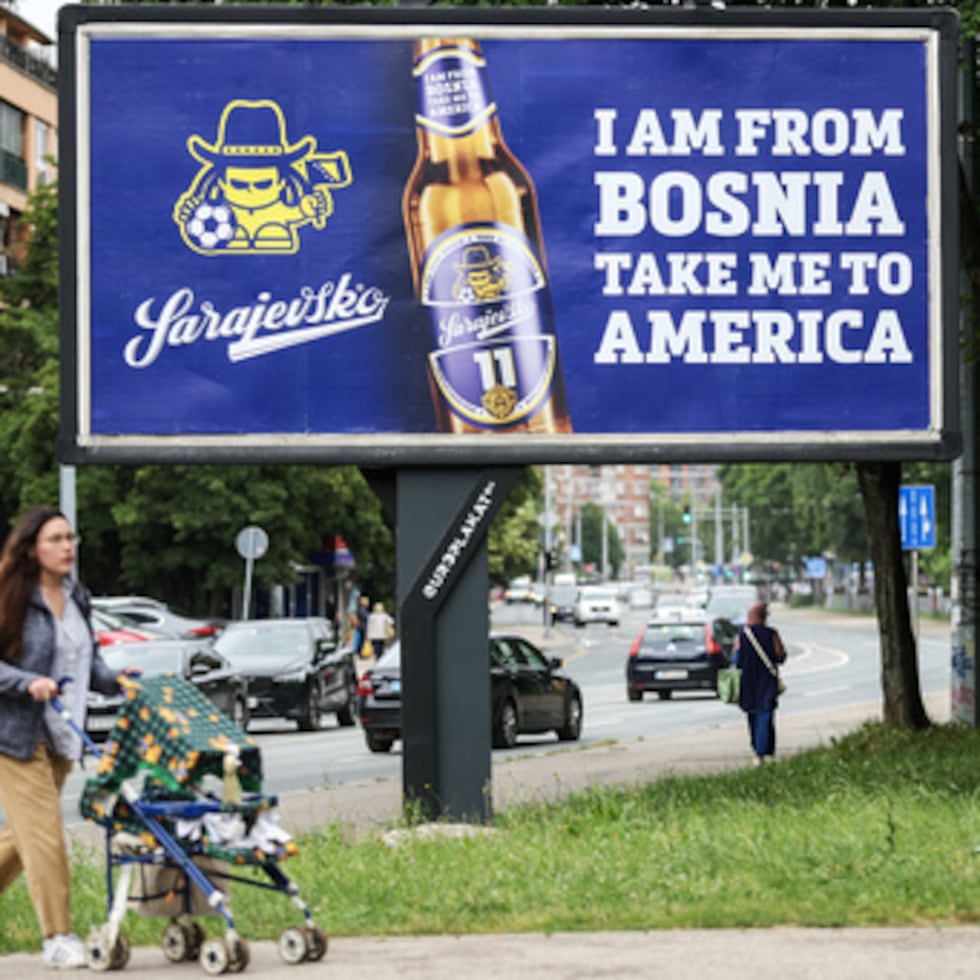 Una mujer pasa junto a una valla publicitaria en la que se muestran la letra de la canción de Dubioza kolektiv «I Am From Bosnia, Take Me to America» en Sarajevo, Bosnia, el jueves 11 de junio de 2026. (Foto AP/Armin Durgut)