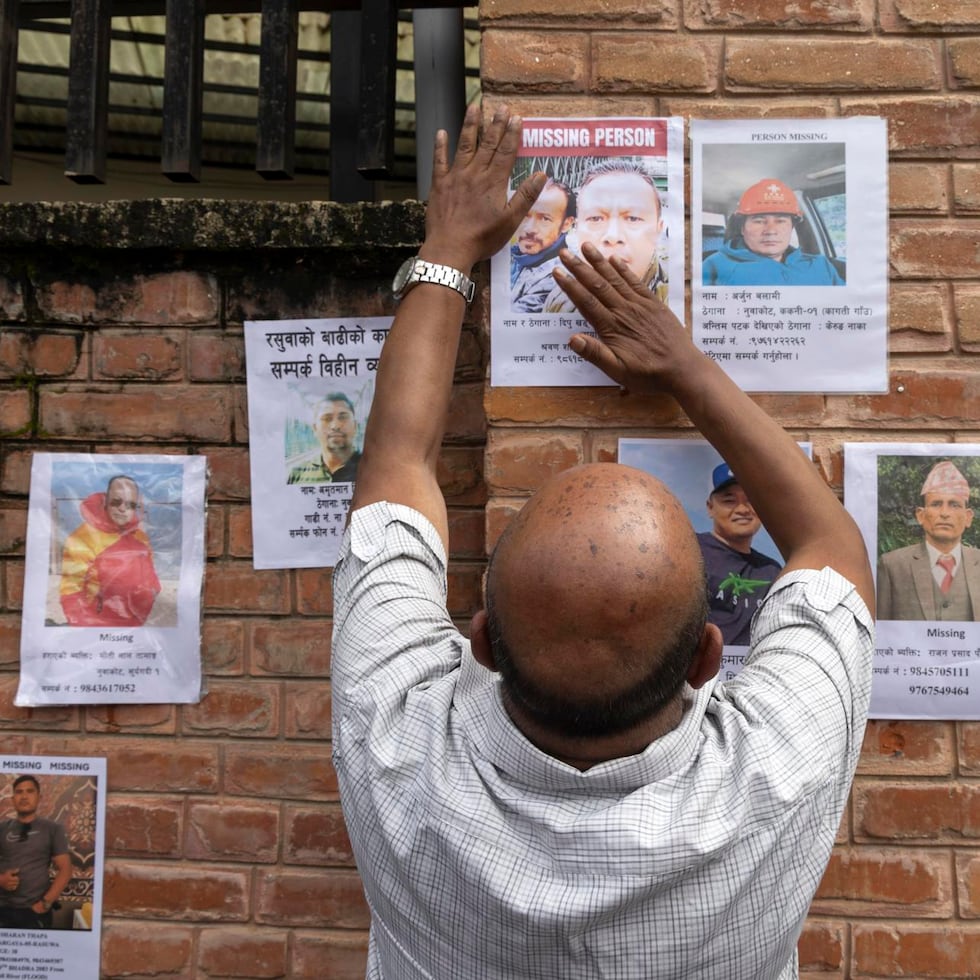 Un hombre coloca un cartel con fotos de personas desaparecidas tras la riada a lo largo de la frontera entre Nepal y el Tíbet en una pared del Hospital Universitario de Tribhuvan (TUTH), en Katmandú.