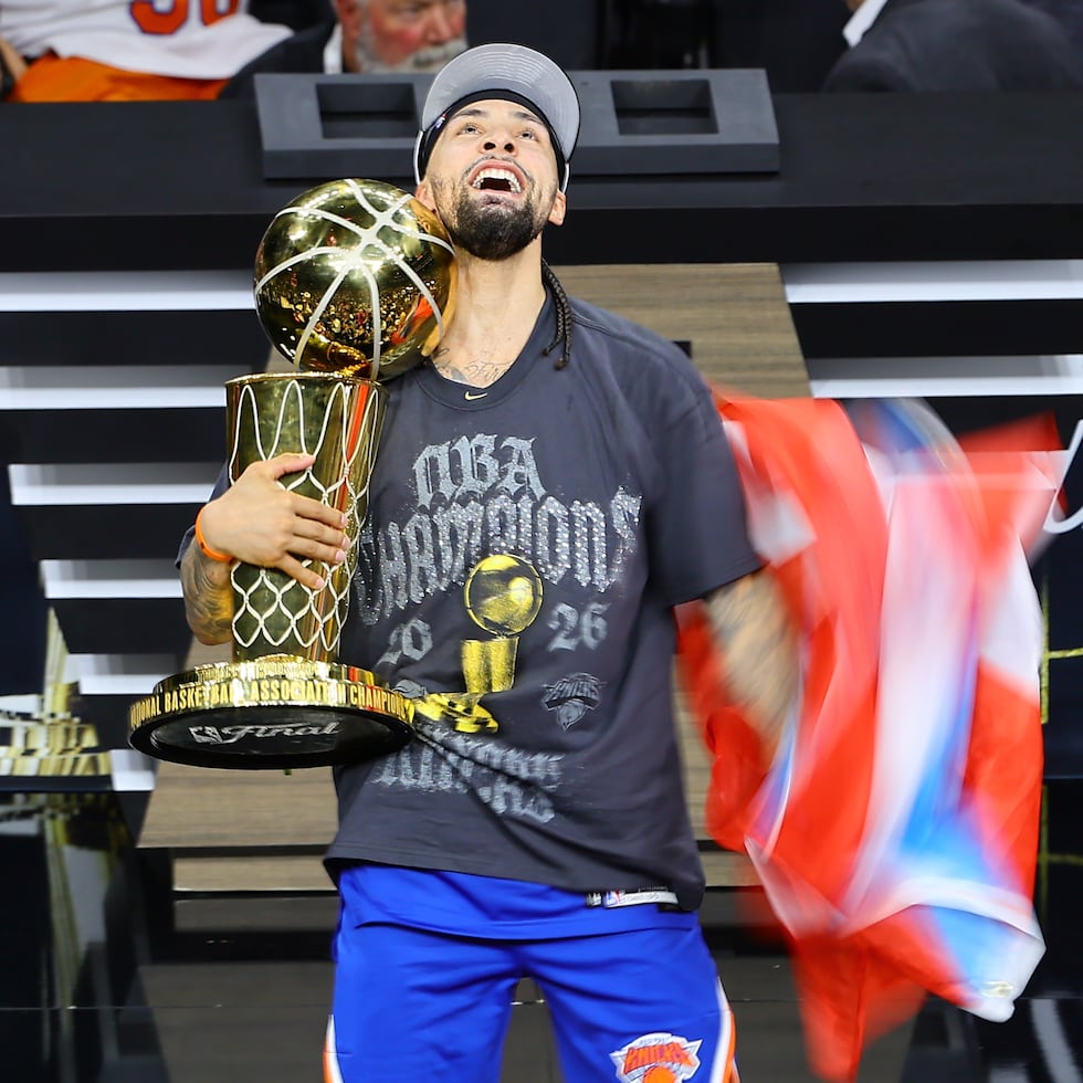El puertorriqueño José Alvarado celebra después de ganar el campeonato de la NBA con los Knicks de Nueva York con el trofeo de campeón y la bandera puertorriqueña.