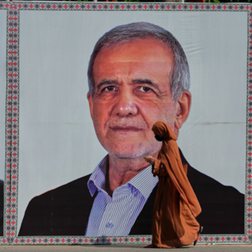 Una mujer camina junto a un cartel de bienvenida con la imagen del presidente de Irán, Masoud Pezeshkian, en Pakistán.