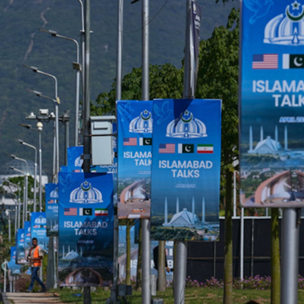 Trabajadores caminan junto a vallas publicitarias cerca del Hotel Serena antes de la segunda ronda de negociaciones entre EE.UU. e Irán, en Islamabad, Pakistán.