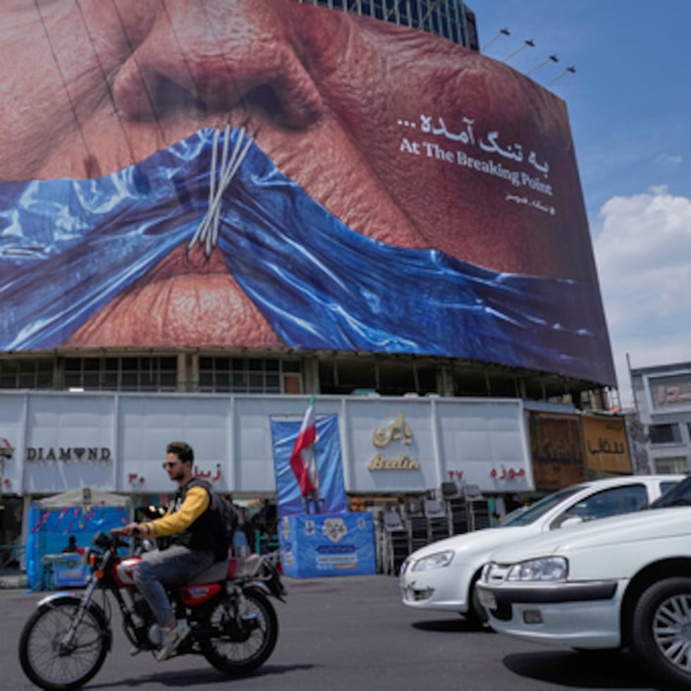 Vehículos pasan junto a una valla publicitaria con un gráfico que muestra el Estrecho de Ormuz y los labios cosidos del presidente estadounidense Donald Trump en una plaza del centro de Teherán, Irán.