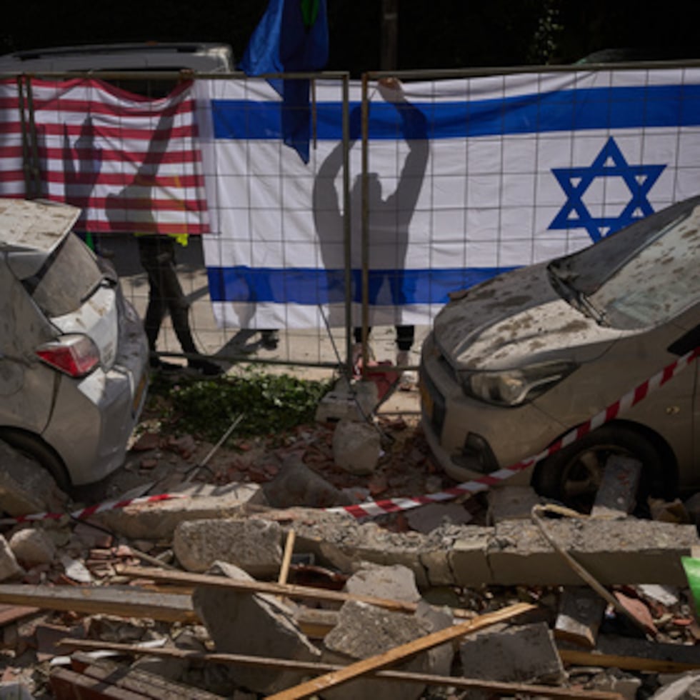 Autoridades israelíes colocan banderas israelíes y estadounidenses en un lugar alcanzado por un misil iraní que mató a dos personas en Ramat Gan, Israel.