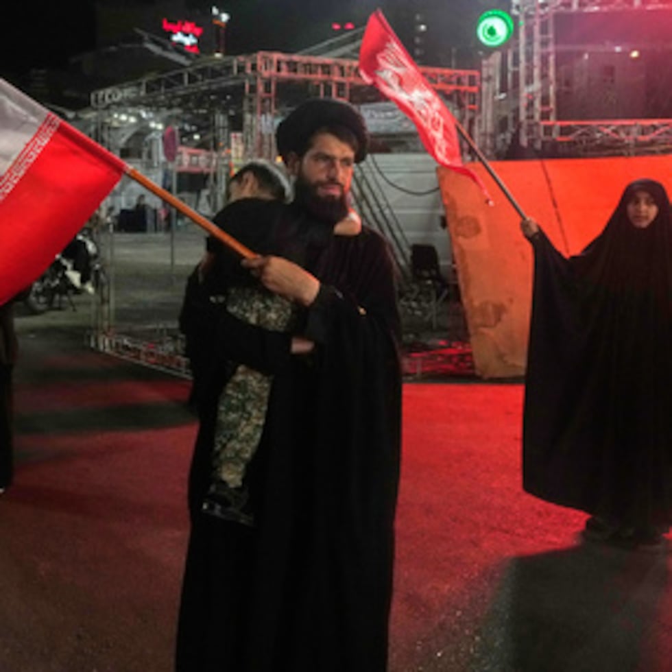 Un clérigo agita una bandera iraní mientras sostiene a un niño en brazos, mientras que una mujer agita una bandera religiosa en una concentración a favor del Gobierno en conmemoración del difunto líder supremo iraní, el ayatolá Alí Jamenei, en una plaza de Teherán, el sábado 11 de julio.