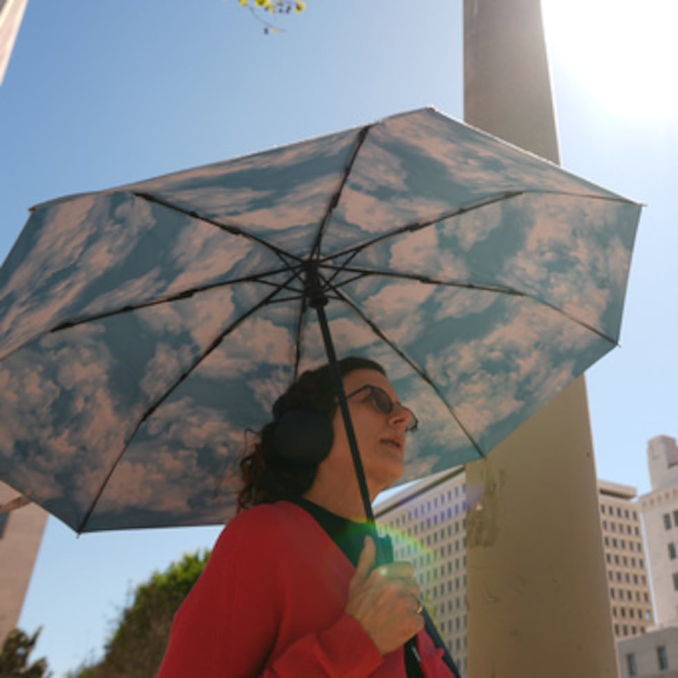 Una ciudadana sostiene un paraguas con temática de nubes bajo un día soleado junto a la alcaldía de Los Ángeles.