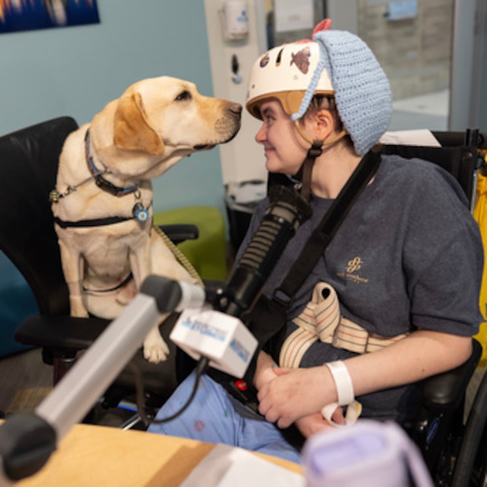 Grover, el perro del Hospital Infantil de Cincinnati, mira a Kira Hodge en los estudios Seacrest del hospital, mientras producen un programa de televisión en circuito cerrado que se transmite a las habitaciones de los pacientes.