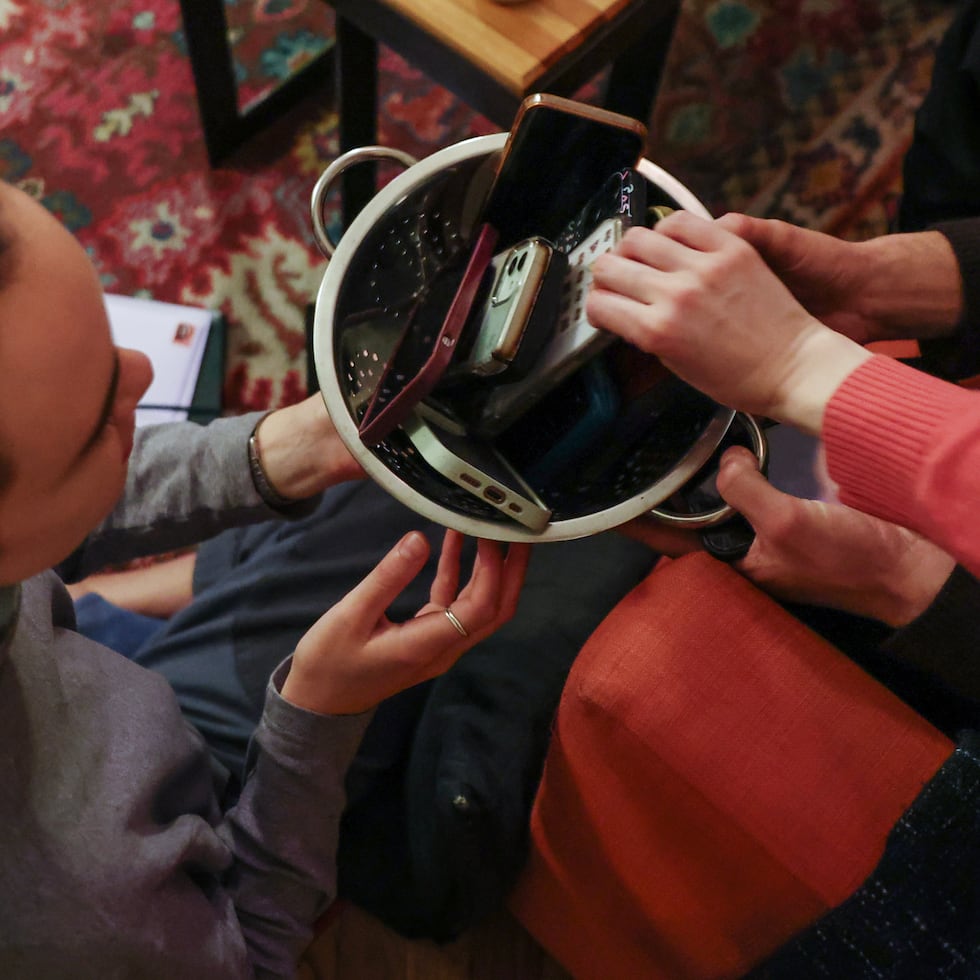 Los participantes de una reunión en que la gente abandona sus teléfonos recogen sus dispositivos de una canasta.