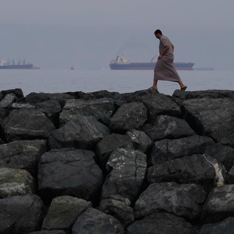 Un hombre camina por la orilla mientras buques petroleros y cargueros se alinean en el estrecho de Ormuz, visto desde Khor Fakkan, Emiratos Árabes Unidos, 11 de marzo de 2026.