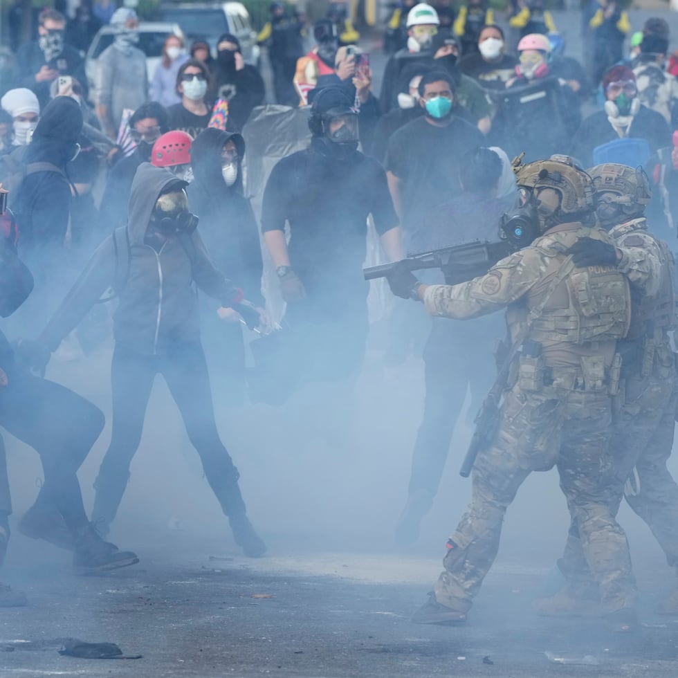 Agentes de la Oficina de Aduanas y Protección Fronteriza de Estados Unidos se enfrentan a manifestantes mientras gases lacrimógenos llenan el aire.