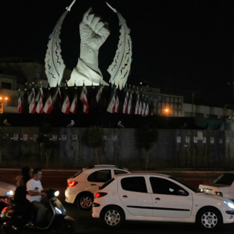 Varios vehículos pasan frente a un monumento que representa el puño cerrado del fallecido líder supremo iraní Alí Jamenei.