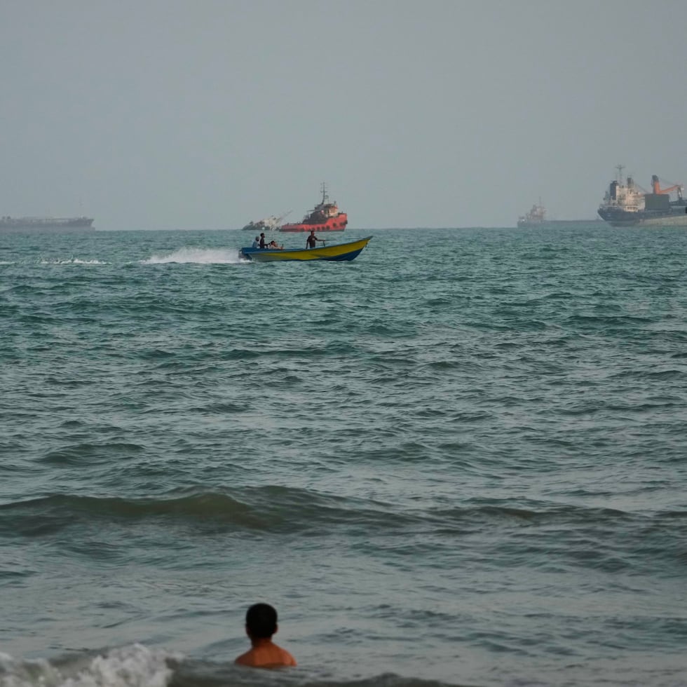 Una persona nada en la costa y al fondo se ven anclados buques en el estrecho de Ormuz, en Bandar Abbas, Irán.