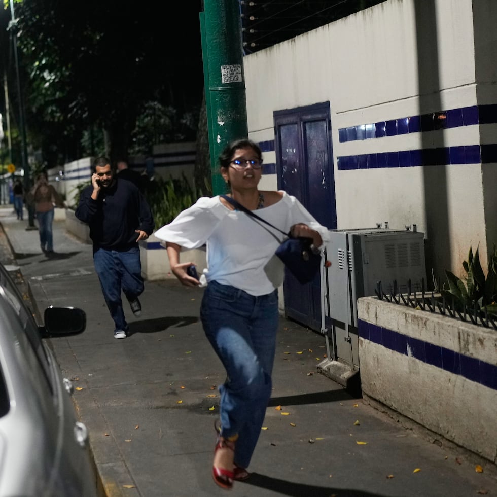 Varias personas corren por una calle tras escuchar explosiones y aviones volando a baja altura en Caracas, capital de Venezuela.