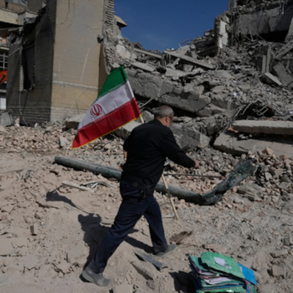 Un hombre se dispone a colocar una bandera de Irán entre los escombros de una comisaría alcanzada por un ataque en la campaña de bombardeos de Estados Unidos e Israel, en Teherán, Irán.