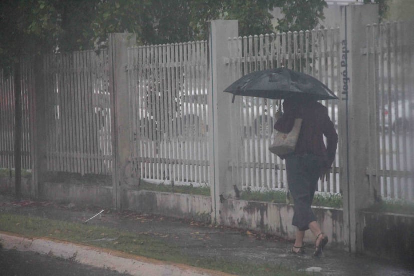 Una mujer camina por una carretera en Hato Rey con sombrilla en mano para evitar mojarse por la lluvia. (GFR Media)