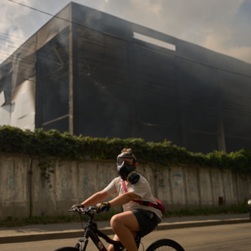 Un residente pasa en bicicleta, con el rostro cubierto por una máscara antigás, frente a un almacén parcialmente destruido por un ataque con drones rusos, en Brovary, a las afueras de Kiev.