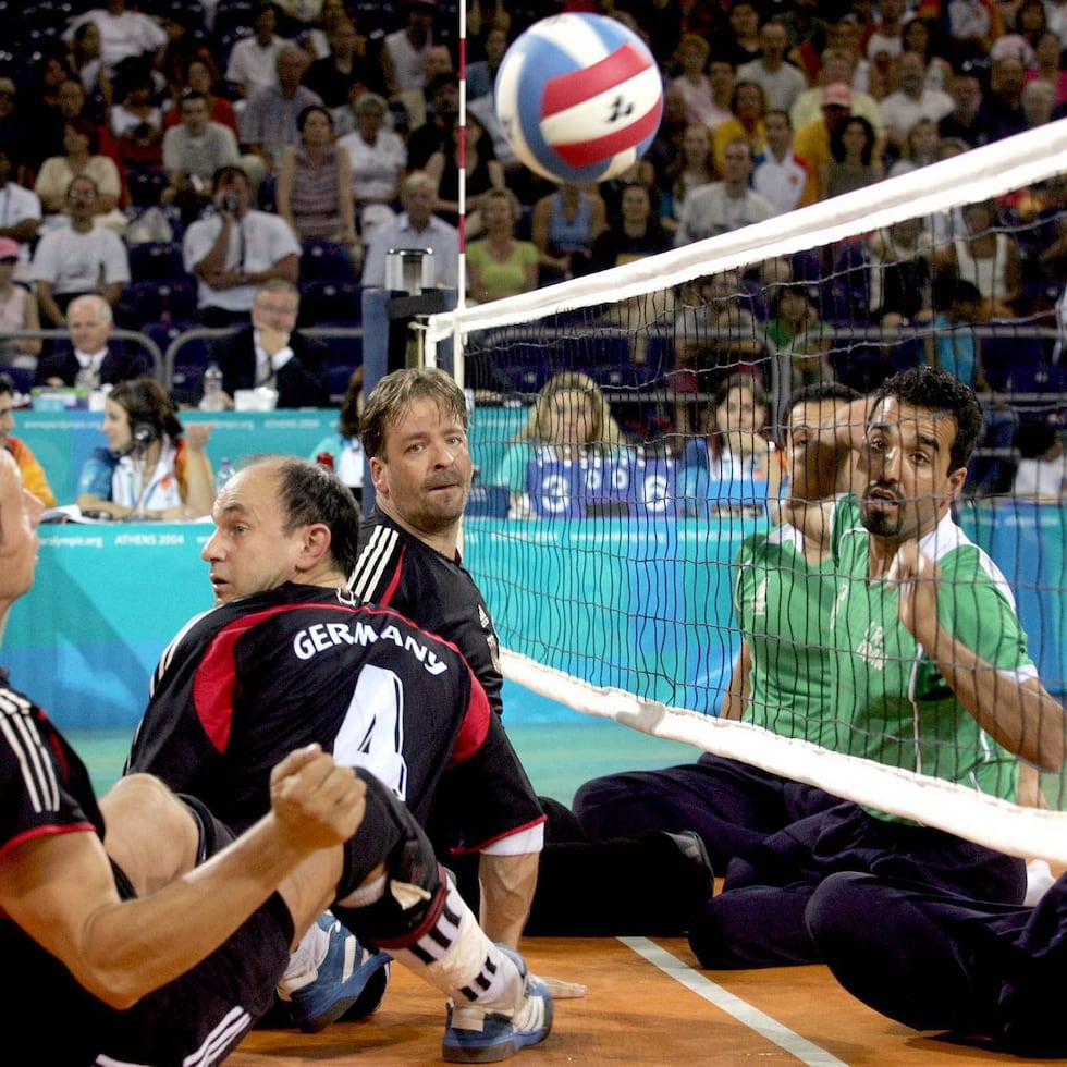 En el voleibol sentado, jugadores con discapacidades físicas compiten sentados en el suelo, en una cancha más pequeña y con la malla colocada más abajo. Sobre estas líneas, imagen de un partido preliminar de voleibol sentado en los Juegos Paralímpicos de Atenas 2004.