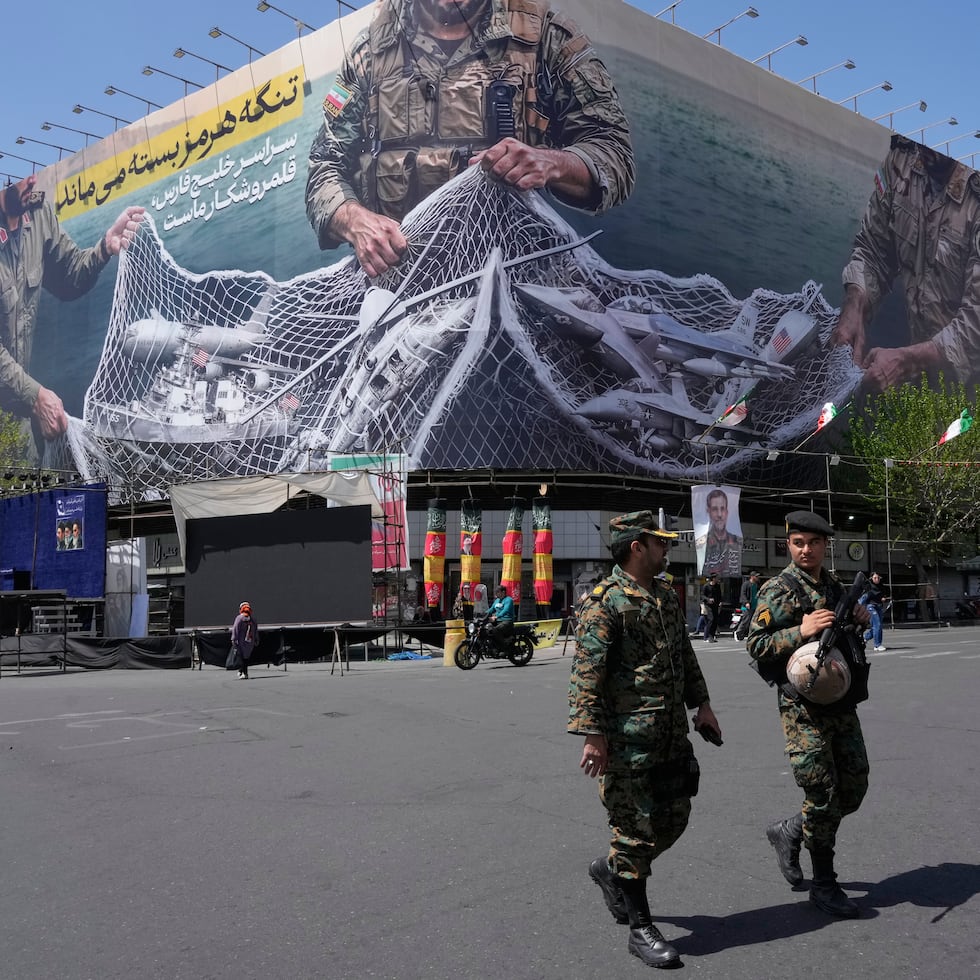 Dos policías caminan frente a una valla publicitaria antiestadounidense que muestra aviones de Estados Unidos siendo capturados por las fuerzas armadas iraníes.