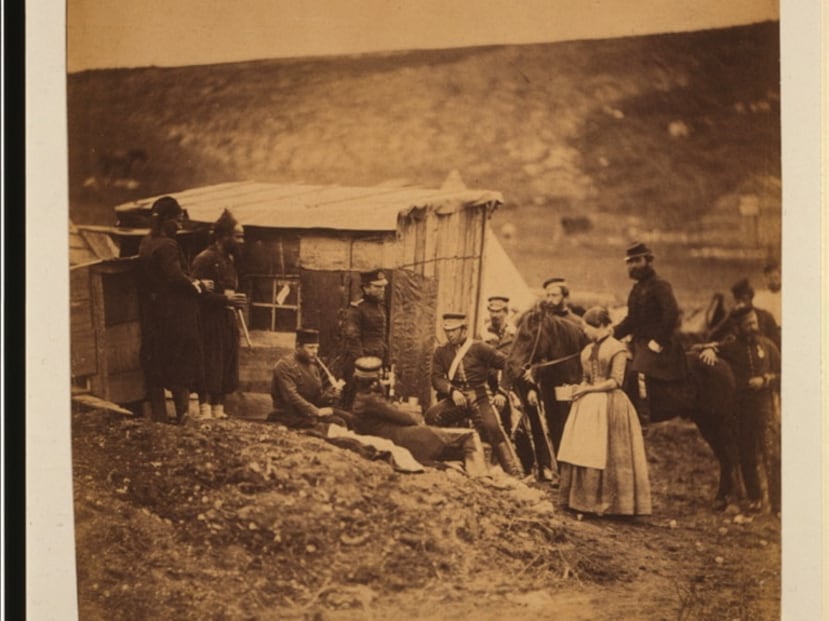 Hombres del 4.º Regimiento de Dragones de la Guardia, uno fumando en pipa, dos zuavos y una mujer (la Sra. Rogers) de pie, sentados o a caballo, frente a la cabaña.