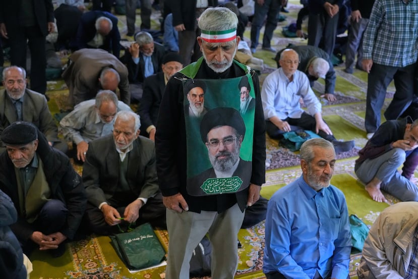An Iranian worshipper wears a banner showing portraits of the Supreme Leader Ayatollah Mojtaba Khamenei, bottom, late Supreme Leader Ayatollah Ali Khamenei, top right, and the late revolutionary founder Ayatollah Khomeini, during Friday prayers ceremony at the Tehran University campus, in Tehran, Iran, Friday, April 24, 2026. (AP Photo/Vahid Salemi)